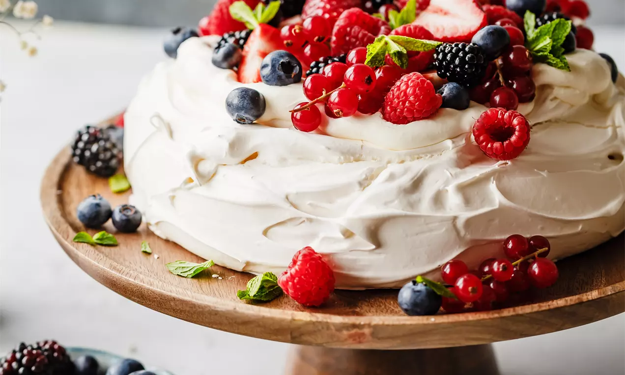 Picture - Witte pavlova met golvende textuur, gegarneerd met rode en blauwe bessen, muntblaadjes op een houten taartplateau