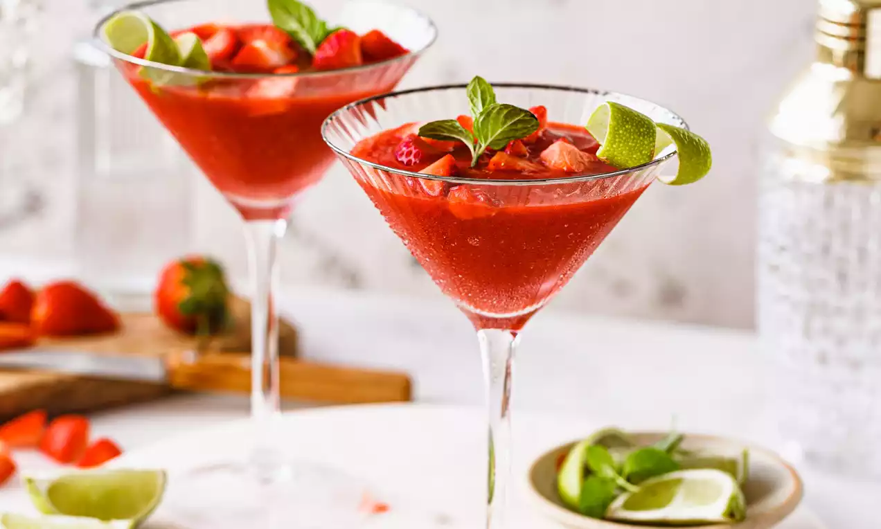 Picture - Twee glazen met felrode aardbei-vanille daiquiri, gegarneerd met munt en limoen, op een wit marmeren bord met verse aardbei en limoen